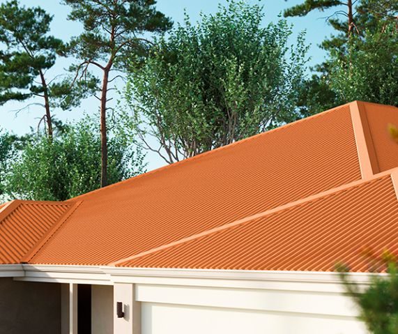 Telhado residencial de várias águas coberto com telha ondulada cor terracota, entre árvores, sob céu azul.